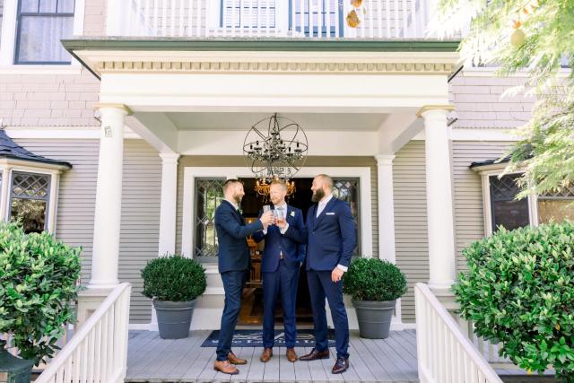 Three men standing on veranda im suites toasting for Sara & James’s Wedding