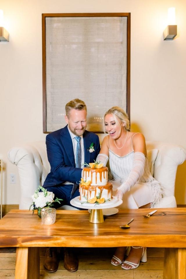 Bride and groom sitting together cutting wedding cake for Sara & James’ Wedding